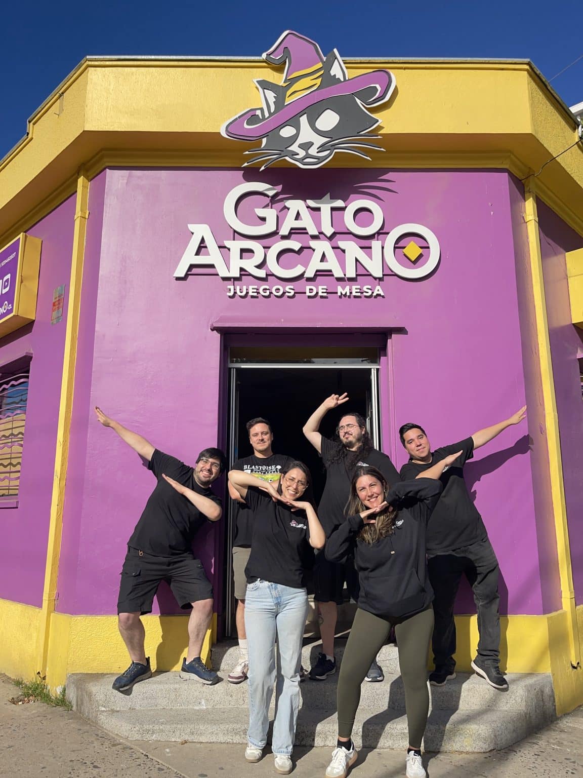 Equipo de Gato Arcano frente a la fachada morada y amarilla